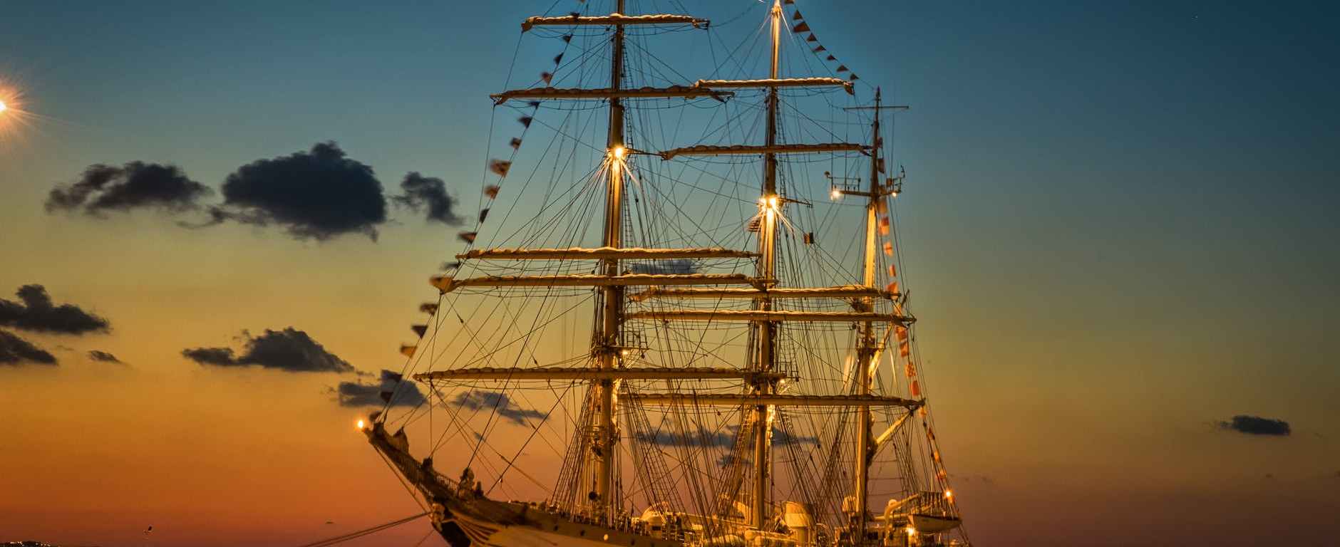 Tall 3-masted ship at sunset anchored with decorative flags