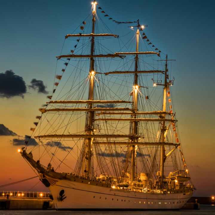 Tall 3-masted ship at sunset anchored with decorative flags