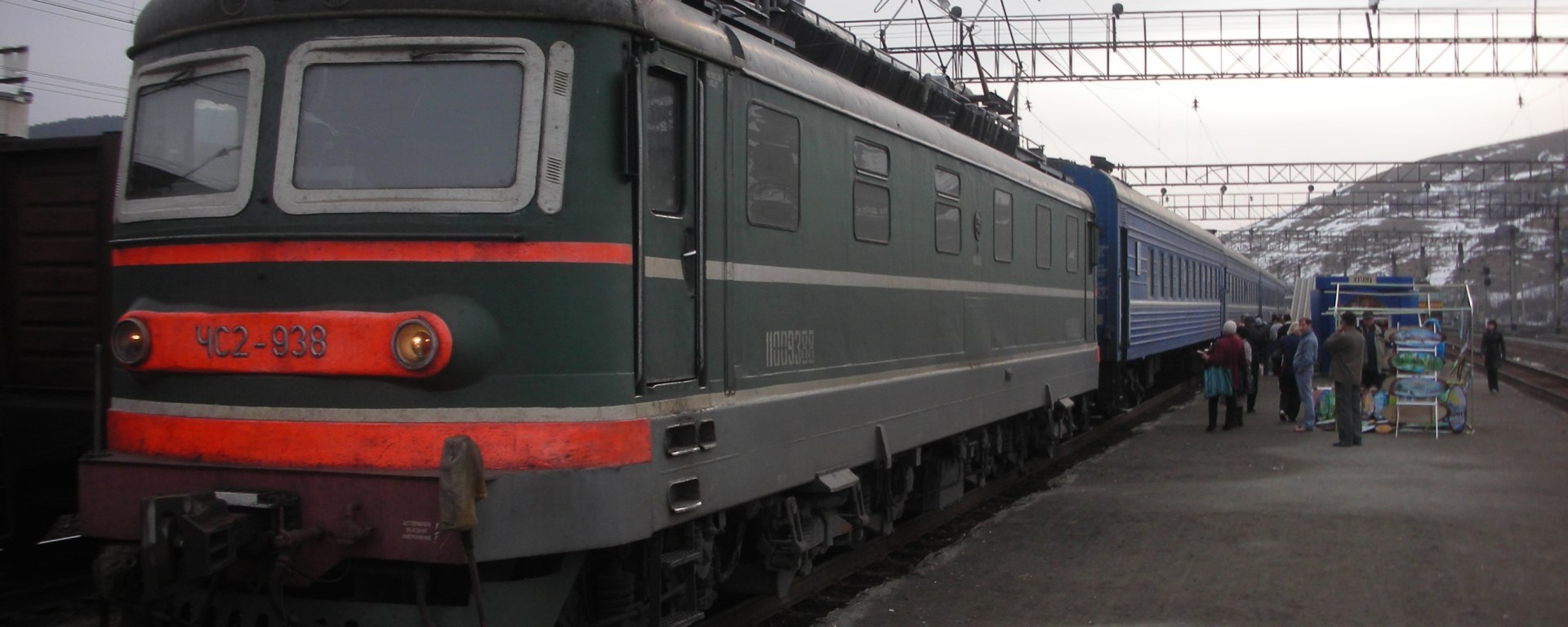 Dark green electric train locomotive pulling a passenger train in the Ural Mountains of Russia