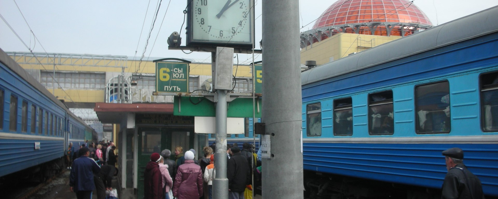 a train station platform in Russia with two waiting passenger trains and clock in foreground